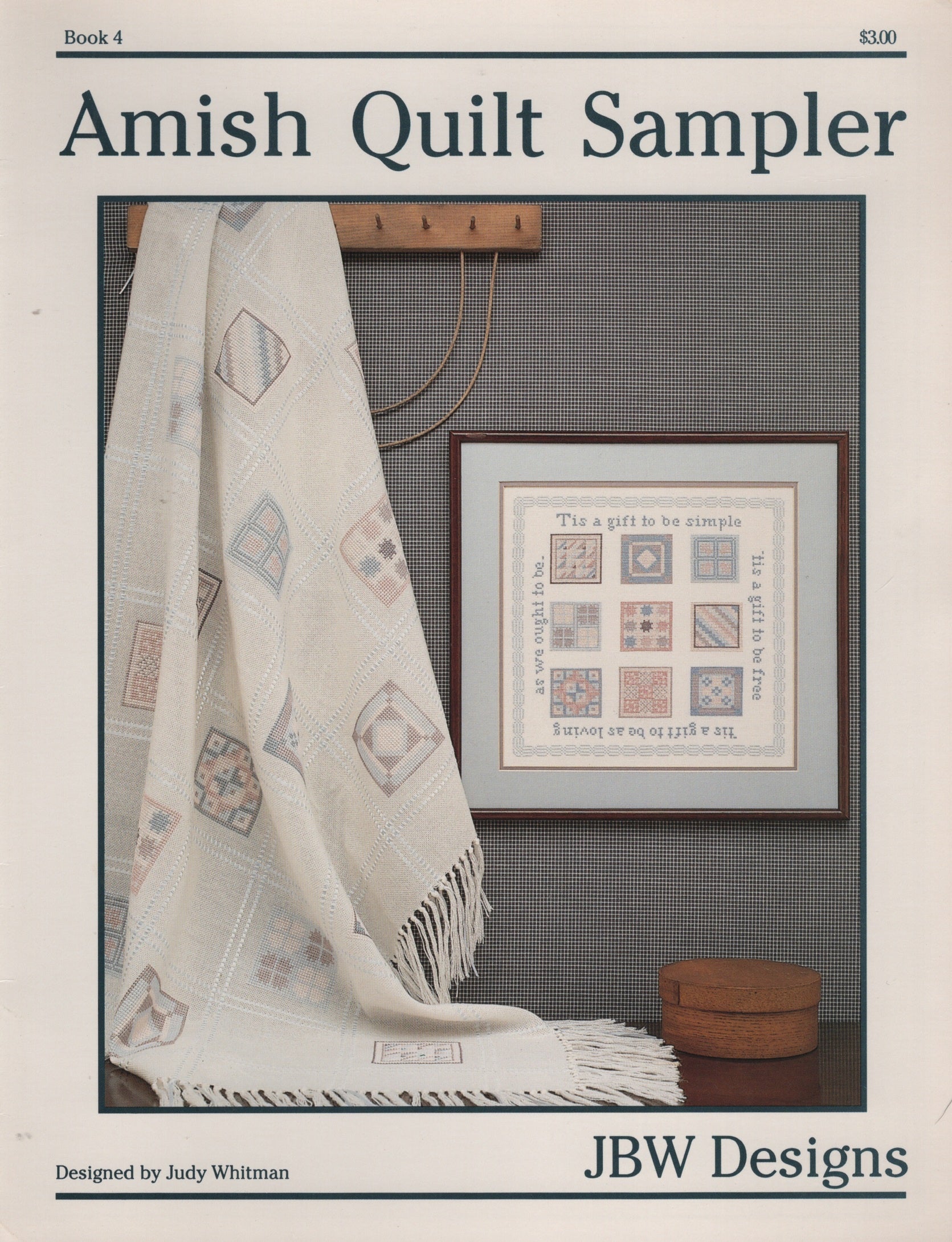 Cover of the Amish Quilt Sampler book by Judy Whitman, published by JBW Designs. The cover features a photograph of an off-white Amish quilt draped over a wall next to a framed cross stitch sampler design. Book 4