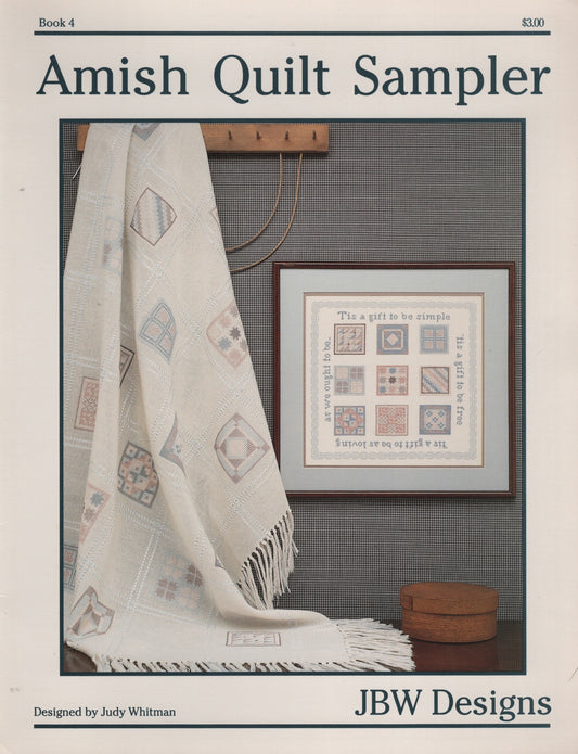 Cover of the Amish Quilt Sampler book by Judy Whitman, published by JBW Designs. The cover features a photograph of an off-white Amish quilt draped over a wall next to a framed cross stitch sampler design. Book 4
