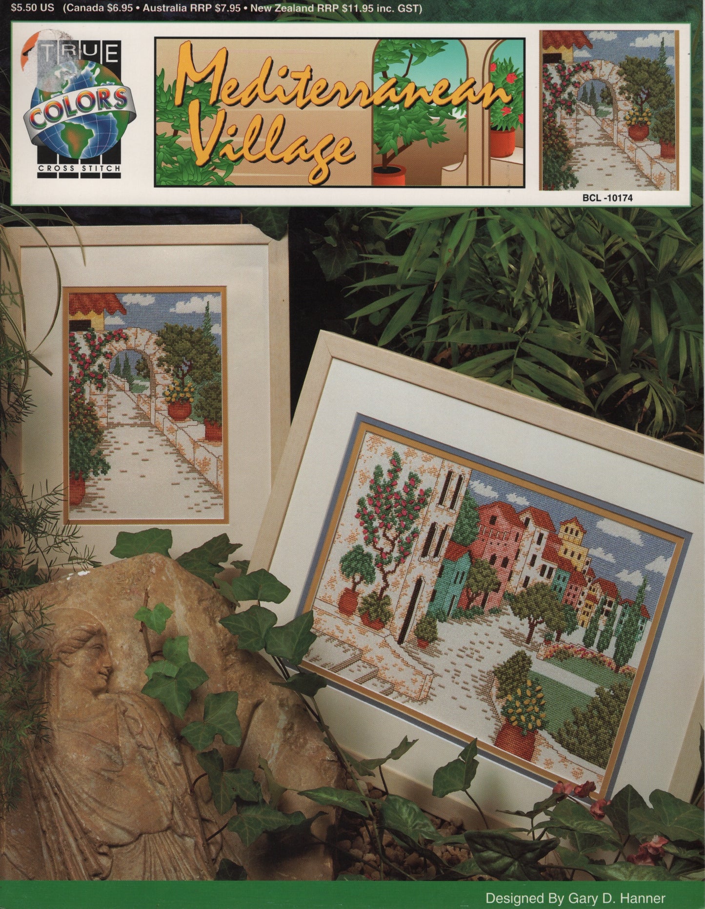 A Mediterranean village scene displayed among green plants and a carved stone. True Colors BCL-10174 cross stitch pattern
