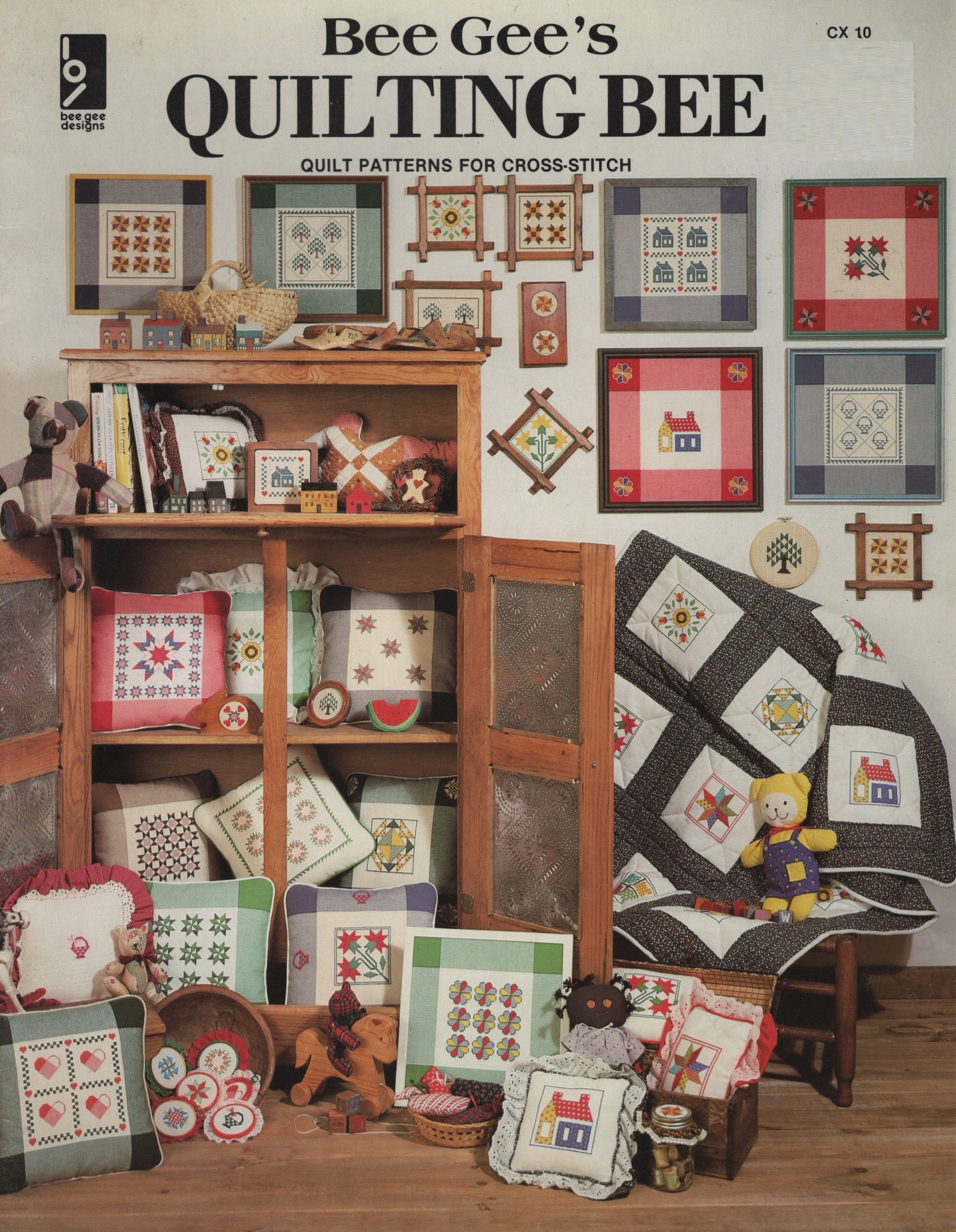 Vintage quilt pattern booklet cover titled 'Bee Gee's Quilting Bee' showing a cozy quilted room scene with patchwork quilts, a wooden cabinet, and stuffed toys. CX10